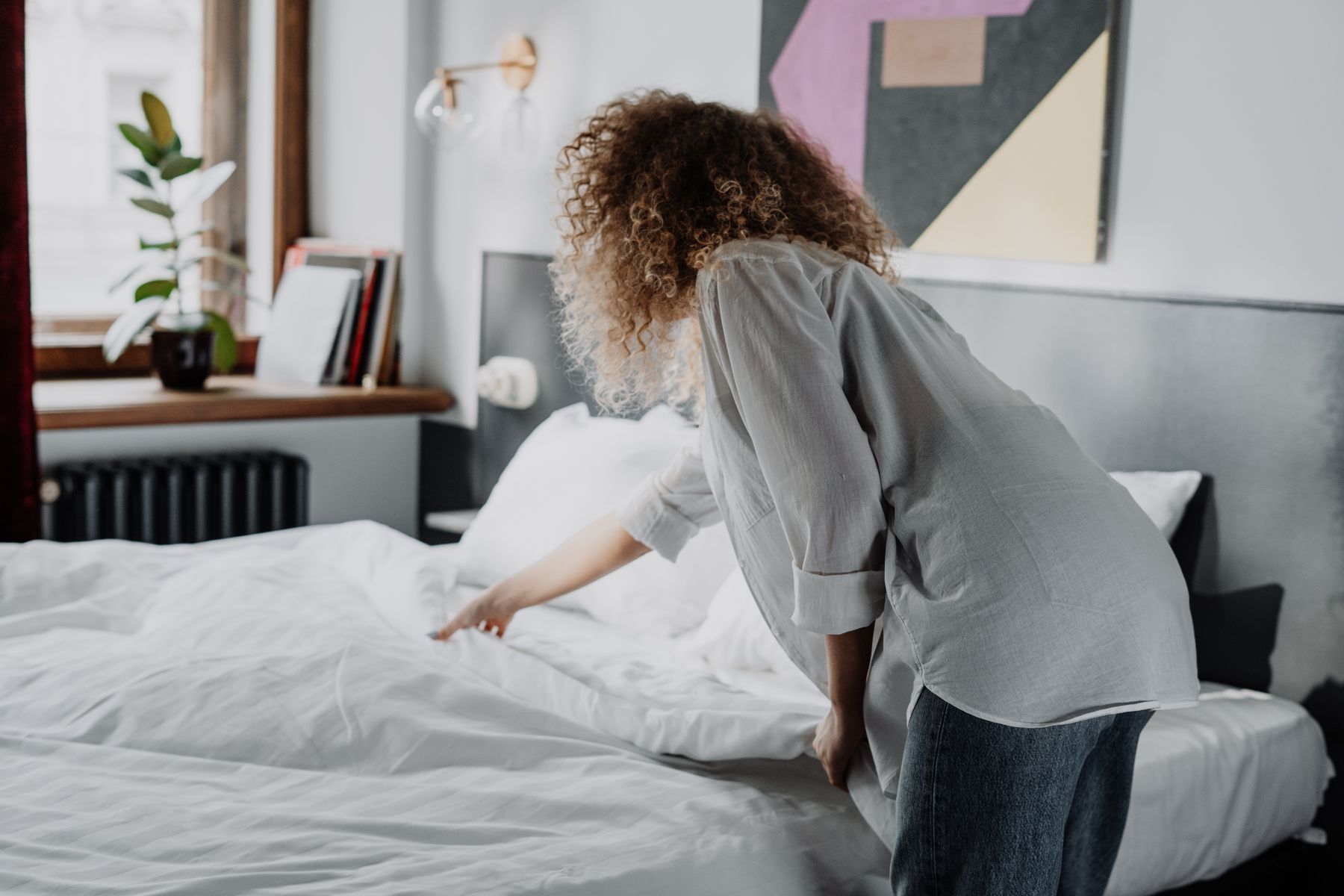 A person making a bed in a bright bedroom