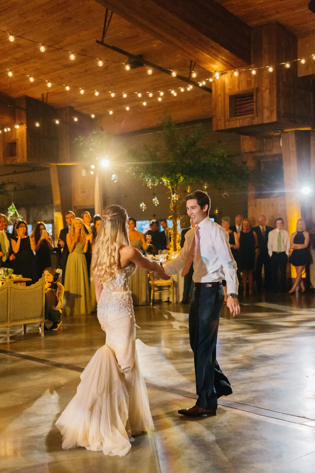 Bride and groom sharing their first dance in a rustic barn venue under string lights
