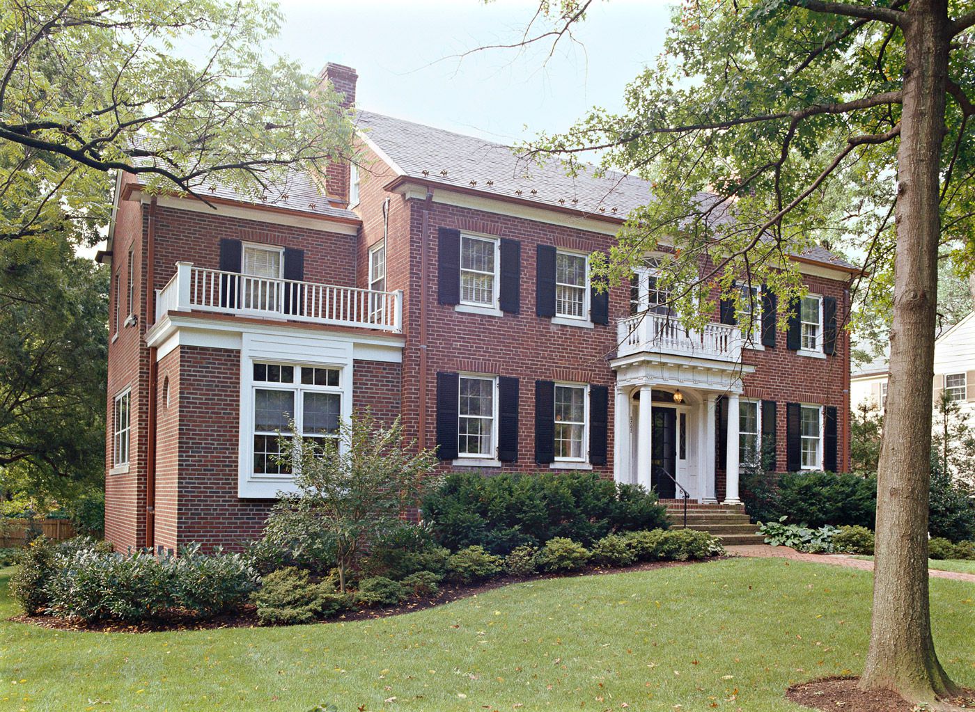 Two-story colonial brick home with white columns and mature landscaping